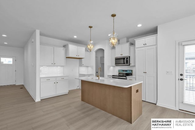 kitchen featuring stainless steel appliances, a kitchen island with sink, hanging light fixtures, and white cabinets