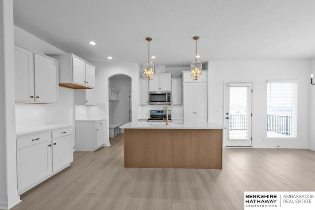 kitchen with a kitchen island with sink, hanging light fixtures, stainless steel appliances, and white cabinets