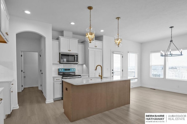 kitchen featuring a kitchen island with sink, decorative light fixtures, tasteful backsplash, and white cabinets