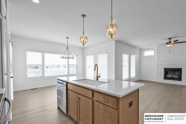 kitchen featuring dishwasher, sink, a large fireplace, hanging light fixtures, and a center island with sink