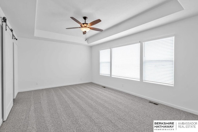 empty room featuring a barn door, ceiling fan, a tray ceiling, and carpet