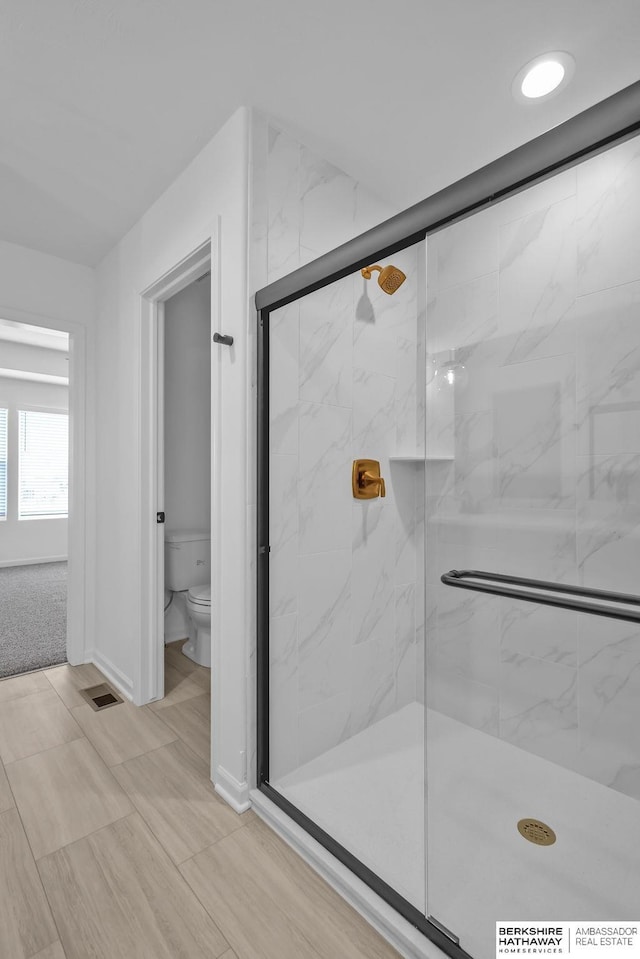 bathroom featuring a shower with door and toilet