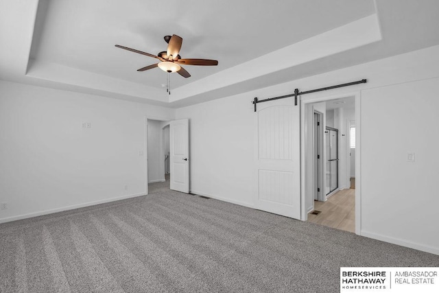 unfurnished room with a tray ceiling, light colored carpet, and a barn door