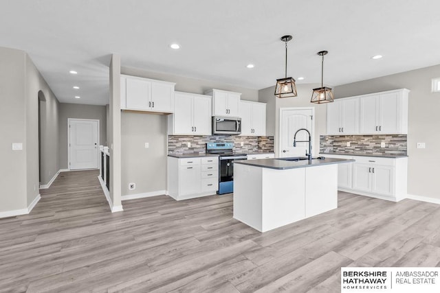 kitchen featuring sink, hanging light fixtures, stainless steel appliances, white cabinets, and a center island with sink