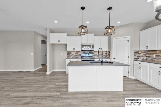 kitchen with stainless steel appliances, a kitchen island with sink, pendant lighting, and white cabinets