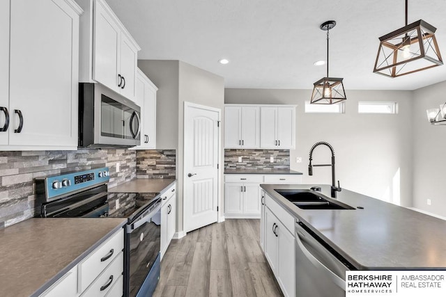 kitchen featuring appliances with stainless steel finishes, pendant lighting, white cabinetry, sink, and light hardwood / wood-style floors