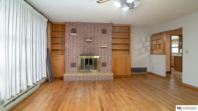 unfurnished living room with built in features, a baseboard heating unit, ceiling fan, a brick fireplace, and light wood-type flooring