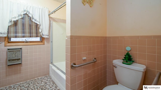 bathroom featuring toilet, tile patterned floors, shower / bath combination with glass door, and tile walls