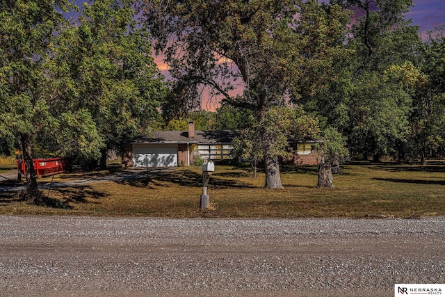 view of property hidden behind natural elements with a garage and a lawn