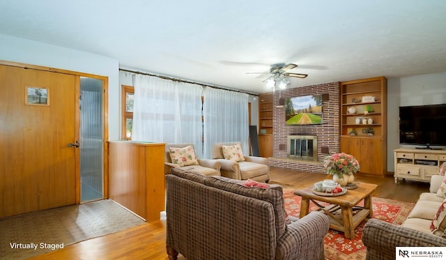 living room with wood-type flooring, ceiling fan, a fireplace, and built in shelves