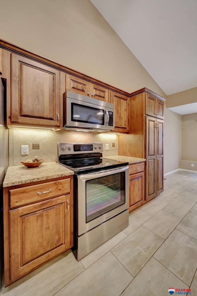 kitchen with vaulted ceiling, appliances with stainless steel finishes, decorative backsplash, light tile patterned floors, and light stone countertops