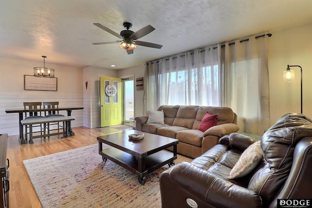 living room featuring ceiling fan with notable chandelier, a textured ceiling, and light wood-type flooring