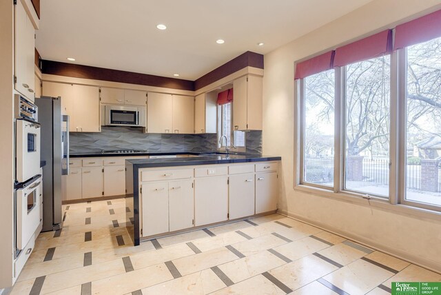 kitchen with backsplash, stainless steel appliances, sink, and white cabinets