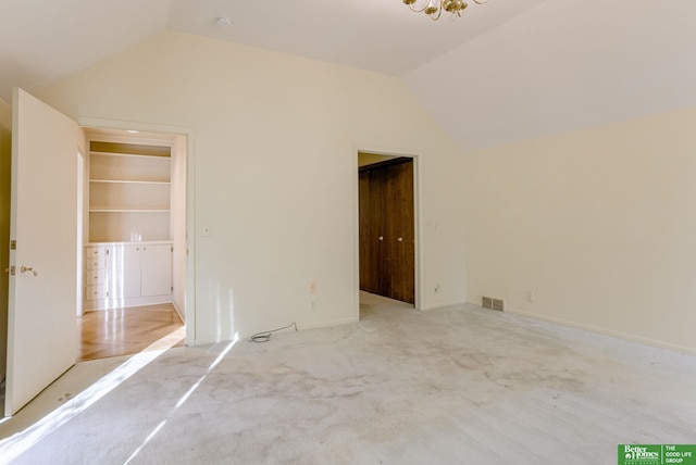 unfurnished bedroom with light colored carpet, vaulted ceiling, and a walk in closet