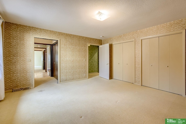 unfurnished bedroom featuring multiple closets, light colored carpet, and a textured ceiling