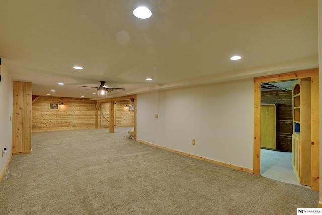 basement featuring ceiling fan, light colored carpet, and wood walls