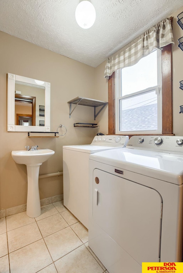 washroom featuring separate washer and dryer, sink, light tile patterned floors, and a textured ceiling