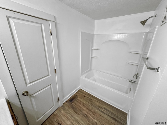 bathroom with wood-type flooring, bathing tub / shower combination, and a textured ceiling