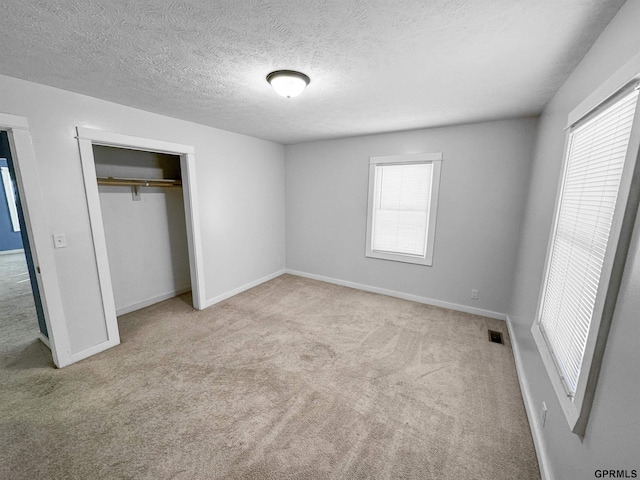 unfurnished bedroom featuring light colored carpet, a textured ceiling, and a closet