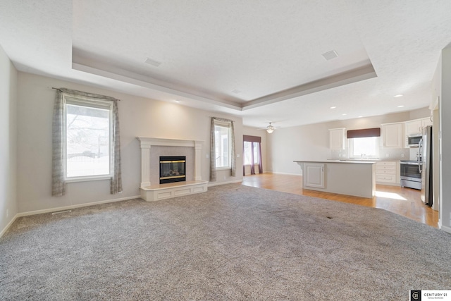 unfurnished living room with a fireplace, light colored carpet, ceiling fan, a tray ceiling, and a textured ceiling