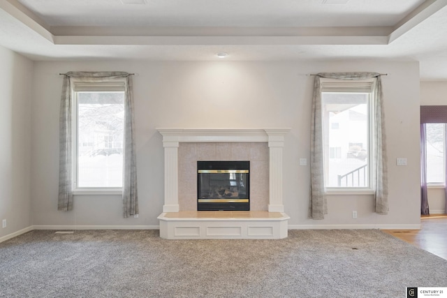 unfurnished living room featuring a tile fireplace, a raised ceiling, and carpet