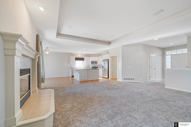 unfurnished living room with a tile fireplace, light carpet, and a tray ceiling