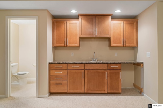 kitchen with sink, light colored carpet, and dark stone counters