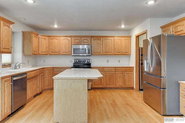 kitchen with appliances with stainless steel finishes, sink, a kitchen island, and light hardwood / wood-style flooring