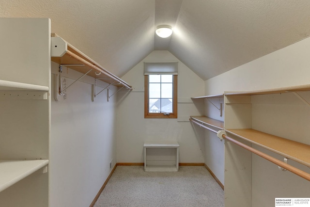 walk in closet with light colored carpet and vaulted ceiling