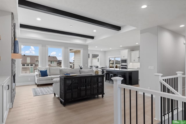 living room with beam ceiling, sink, and light wood-type flooring