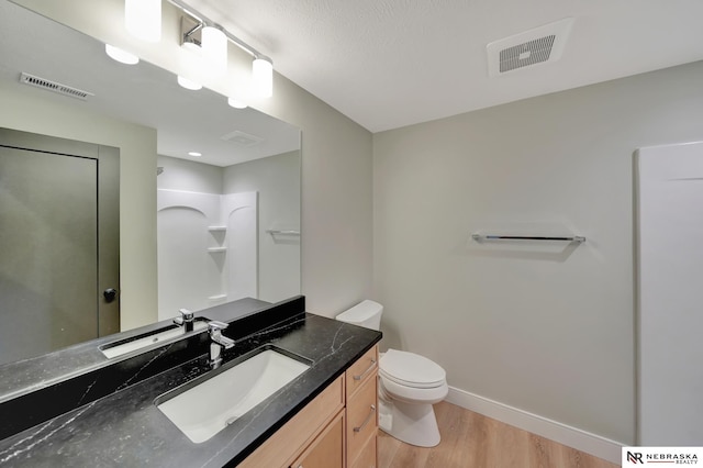 bathroom with hardwood / wood-style flooring, vanity, toilet, and a shower