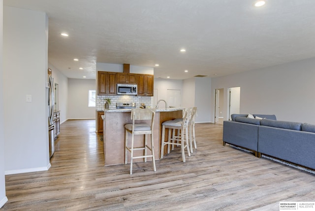 kitchen featuring tasteful backsplash, a breakfast bar area, light hardwood / wood-style floors, stainless steel appliances, and light stone countertops