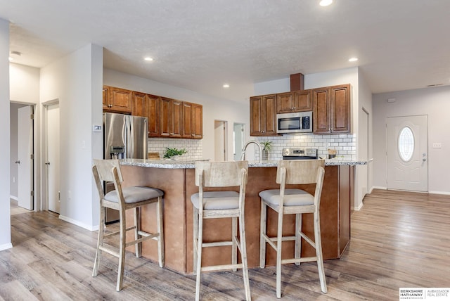 kitchen with stainless steel appliances, a kitchen bar, light wood-type flooring, and light stone counters