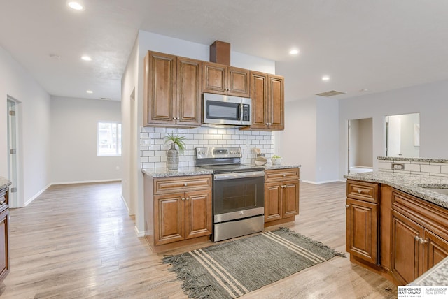 kitchen featuring light stone counters, tasteful backsplash, light hardwood / wood-style flooring, and appliances with stainless steel finishes