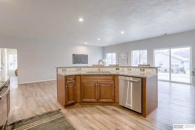 kitchen featuring sink, light stone counters, light hardwood / wood-style flooring, dishwasher, and an island with sink