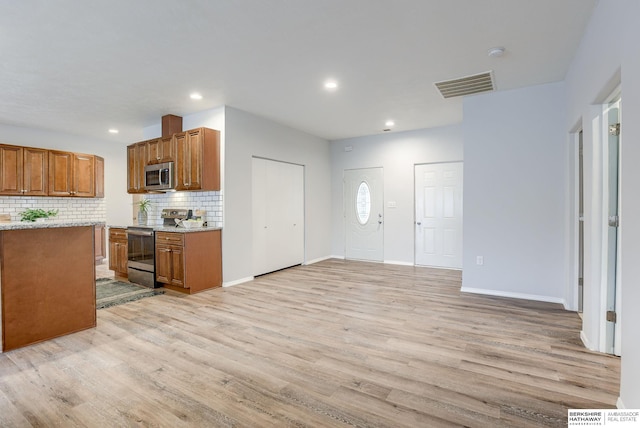 kitchen with appliances with stainless steel finishes, light wood-type flooring, and decorative backsplash