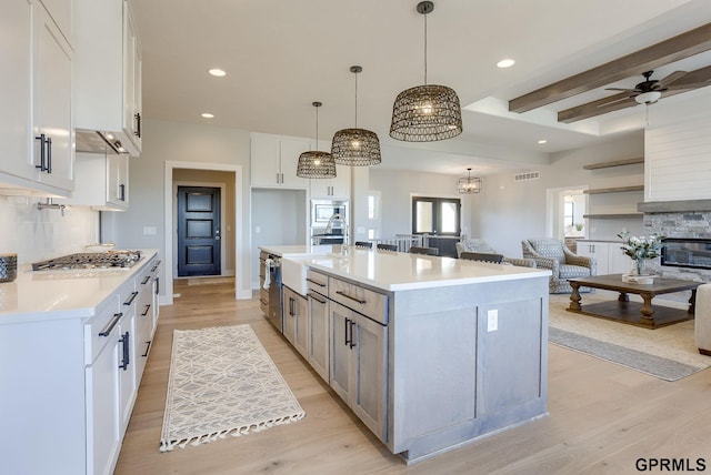 kitchen with light hardwood / wood-style flooring, decorative backsplash, white cabinets, decorative light fixtures, and a large island with sink