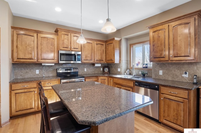 kitchen with sink, a kitchen island, pendant lighting, stainless steel appliances, and light hardwood / wood-style floors