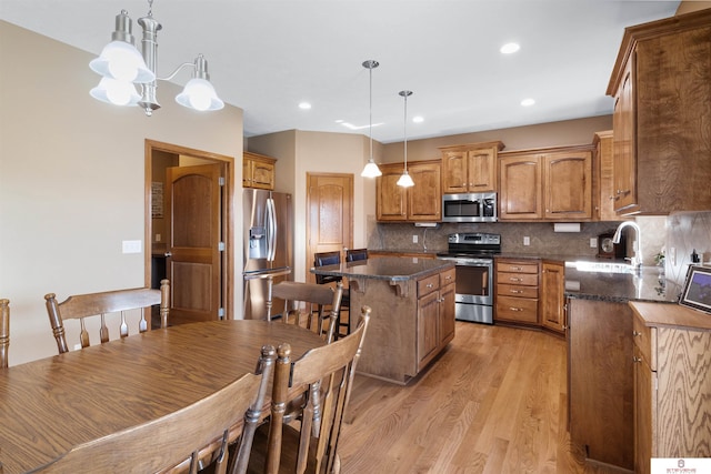 kitchen with appliances with stainless steel finishes, sink, hanging light fixtures, a center island, and light wood-type flooring