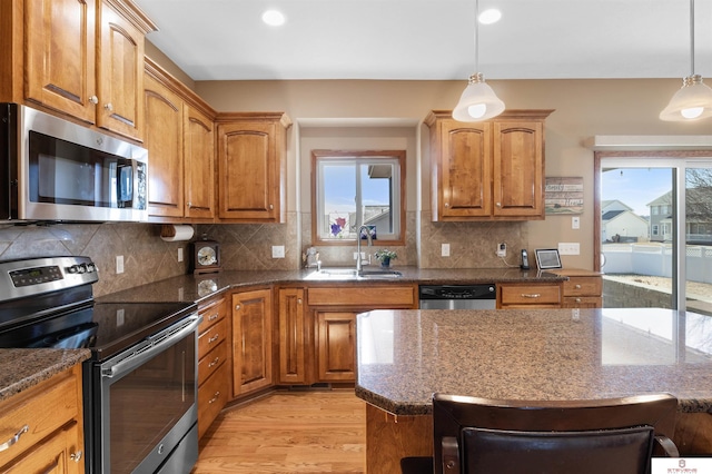 kitchen featuring a wealth of natural light, decorative light fixtures, sink, dark stone countertops, and stainless steel appliances