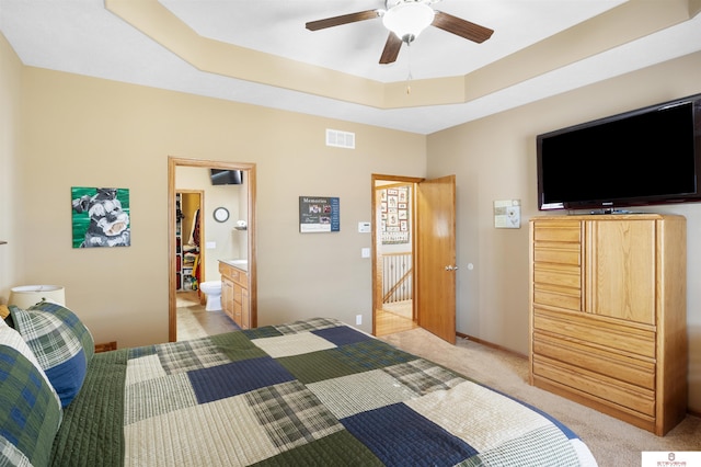 carpeted bedroom with ensuite bath, a raised ceiling, and ceiling fan