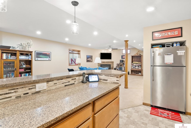 kitchen featuring a stone fireplace, stainless steel fridge, pendant lighting, ceiling fan, and light stone countertops