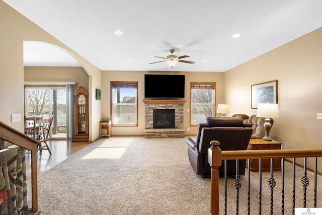 carpeted living room featuring ceiling fan and a stone fireplace