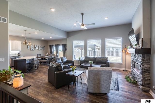 living room with ceiling fan, dark hardwood / wood-style floors, a stone fireplace, and a textured ceiling