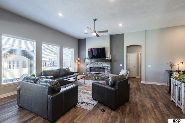 living room with a stone fireplace, dark wood-type flooring, and ceiling fan