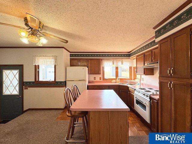 kitchen with a kitchen island, a kitchen bar, white appliances, crown molding, and a textured ceiling