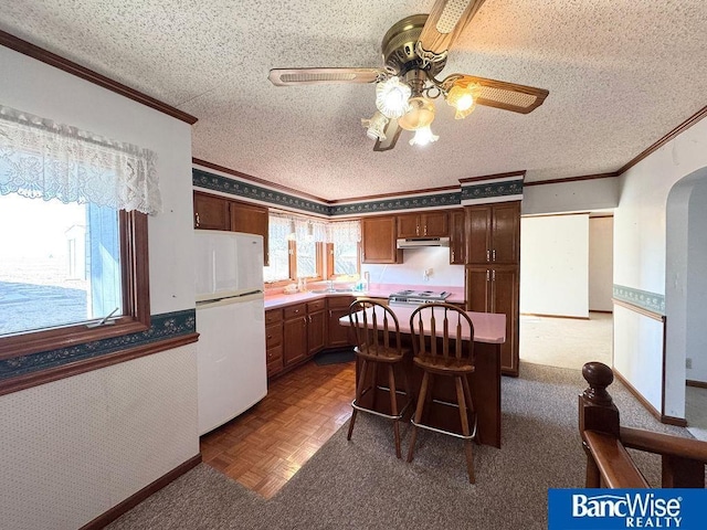 kitchen featuring ornamental molding, a kitchen breakfast bar, white fridge, and a textured ceiling