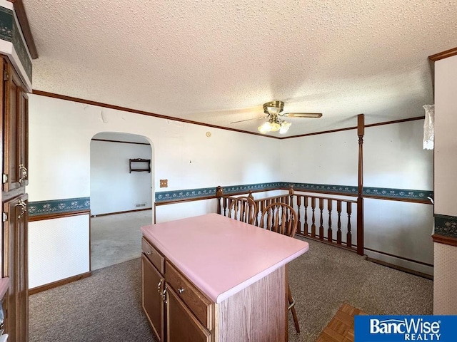 interior space with a textured ceiling, ornamental molding, a center island, and ceiling fan