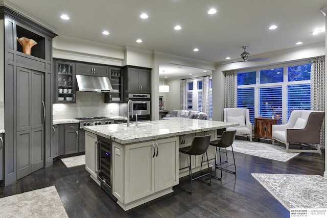 kitchen with gray cabinets, a kitchen island with sink, stainless steel appliances, wine cooler, and dark hardwood / wood-style flooring