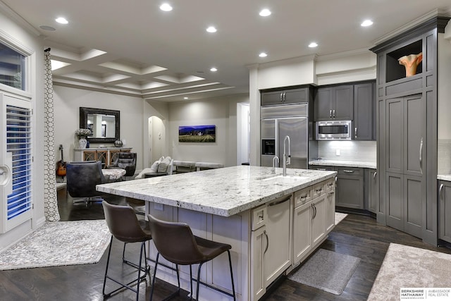 kitchen with gray cabinetry, a kitchen breakfast bar, decorative backsplash, built in appliances, and a center island with sink